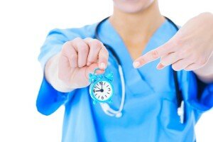 Midsection Of Nurse Pointing At Toy Alarm Clock